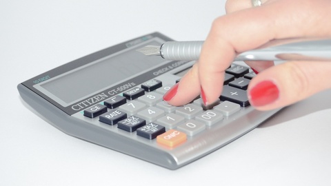 Image d'illustration : une main tape un calcul sur une calculatrice à grosses touches tout en tenant un stylo plume.