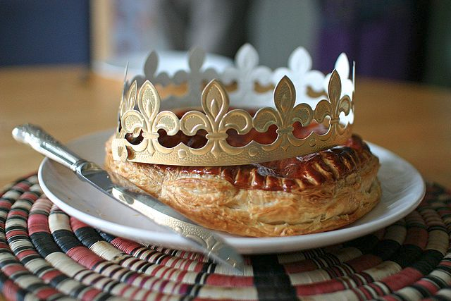Galette des rois surmontée d'une couronne dorée en papier et posée dans une assiette blanche. Un couteau est posé sur l'assiette à côté de la galette.